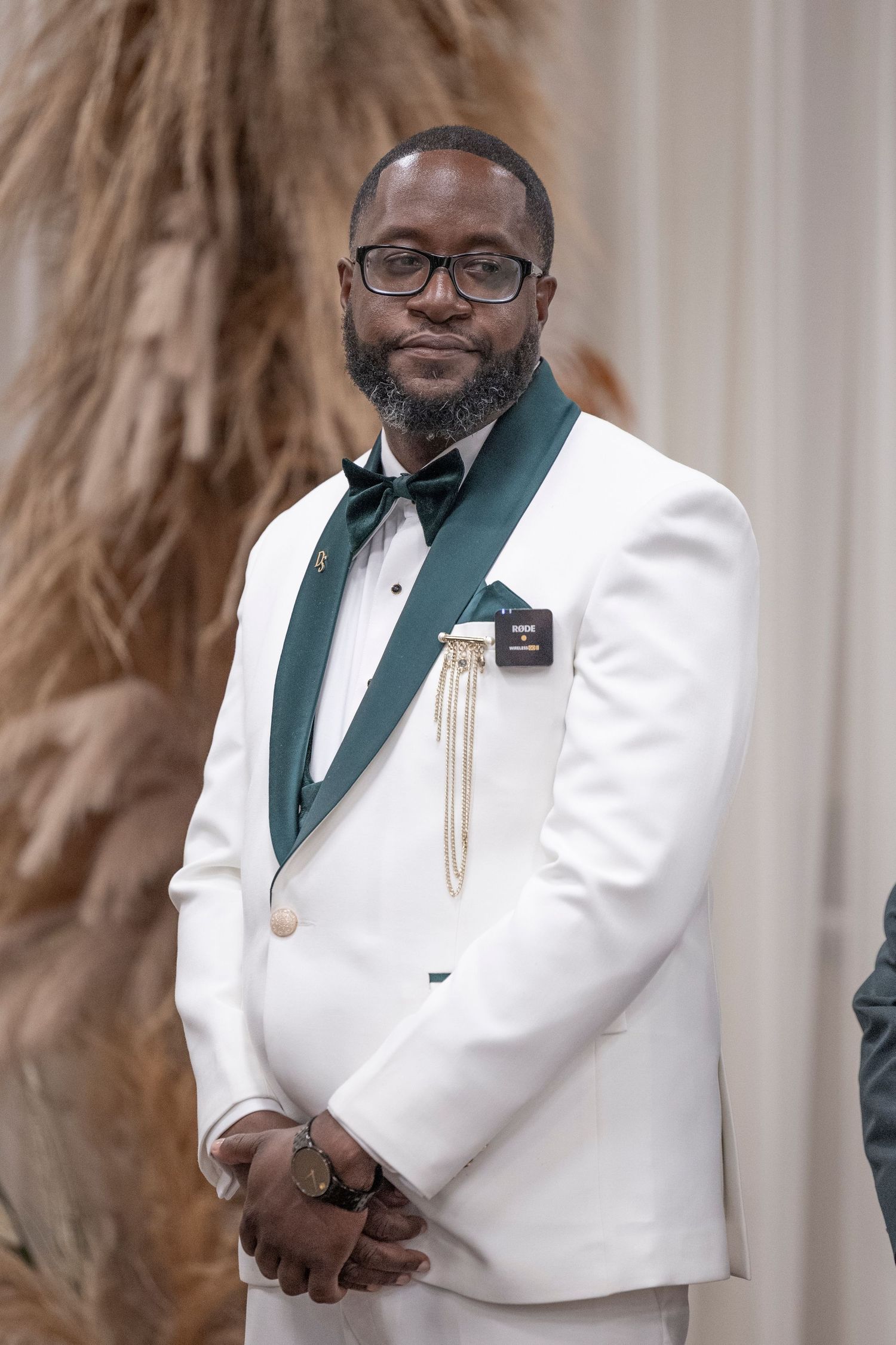 Man in white tuxedo jacket and dark green shawl lapel poses for formal portrait with glasses.
