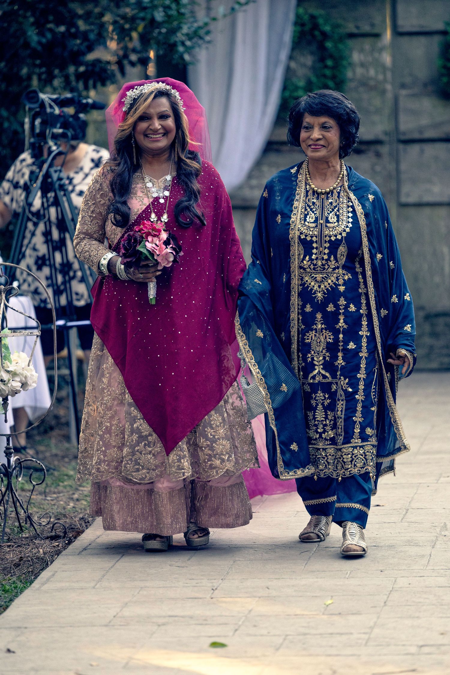 Two people in traditional South Asian formal attire walking together on a stone pathway.