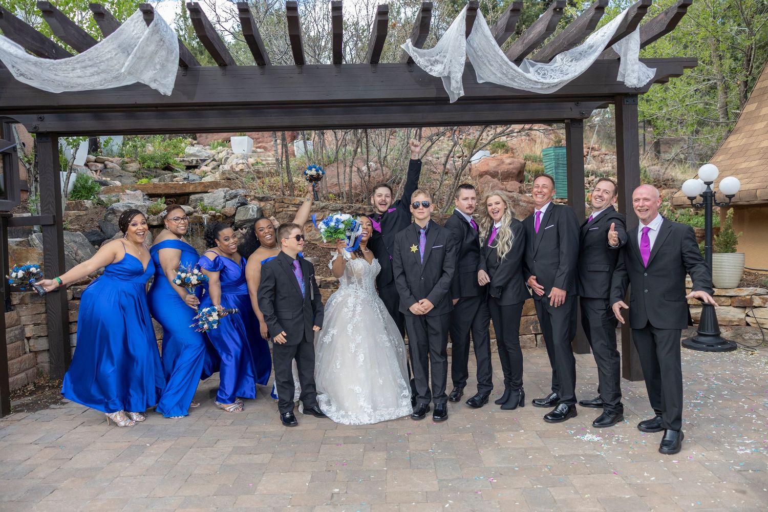 Wedding party in formal attire poses together on outdoor stone patio during celebration.