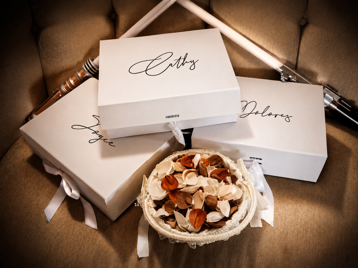 White personalized gift boxes with elegant script names beside a bowl of mixed nuts on a beige surface.