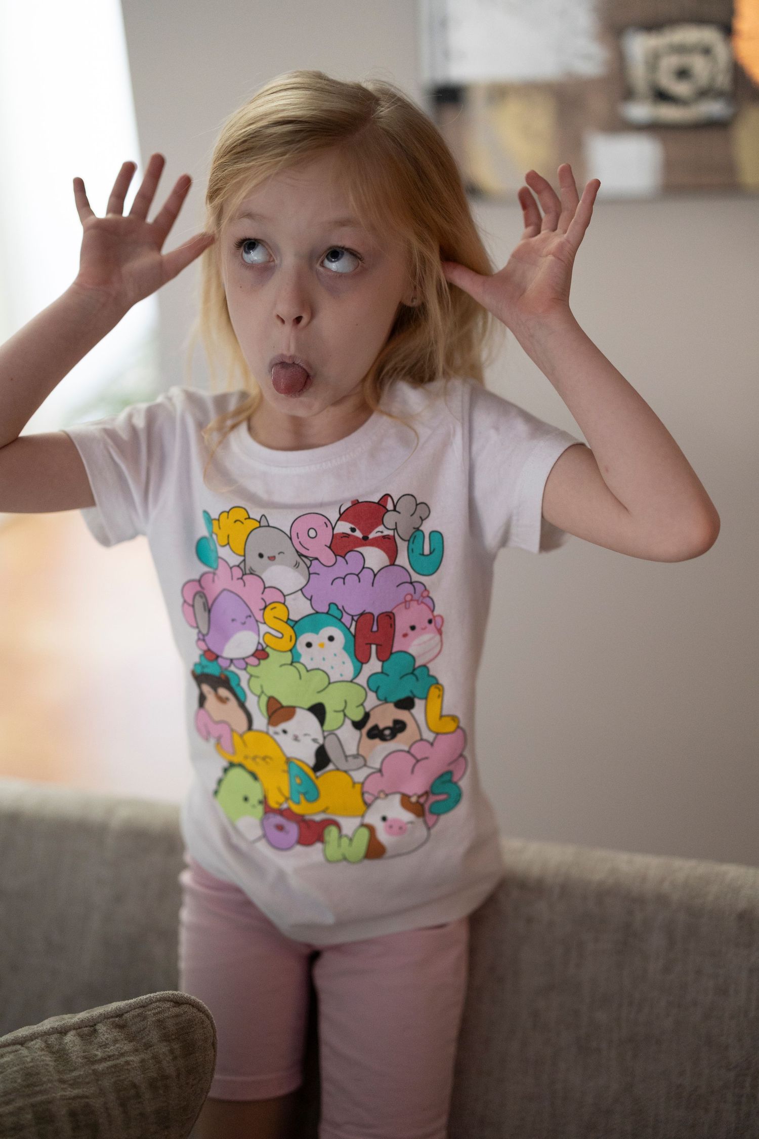 A playful child wearing a colorful cartoon character t-shirt makes a silly face with hands raised.