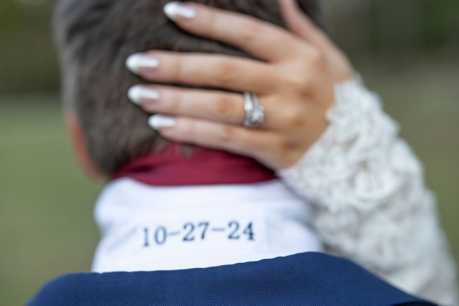 A close-up view of hands holding a white lace wedding dress fabric against a blurred green background.