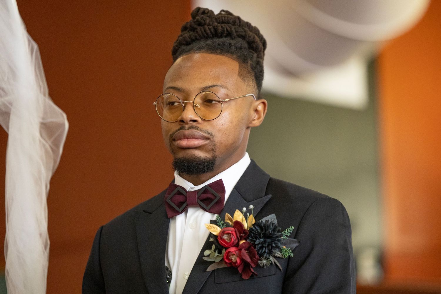 A well-dressed wedding attendee in a black tuxedo with burgundy bow tie and floral boutonniere.