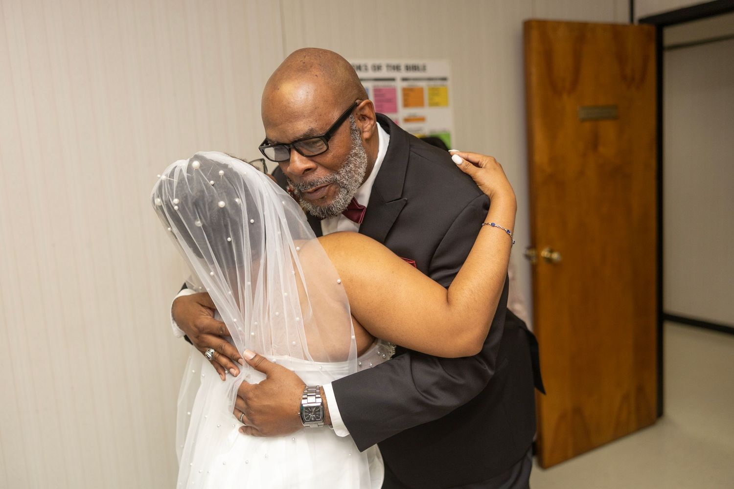 Couple sharing a tender embrace during an emotional wedding moment in a warm-lit indoor setting.