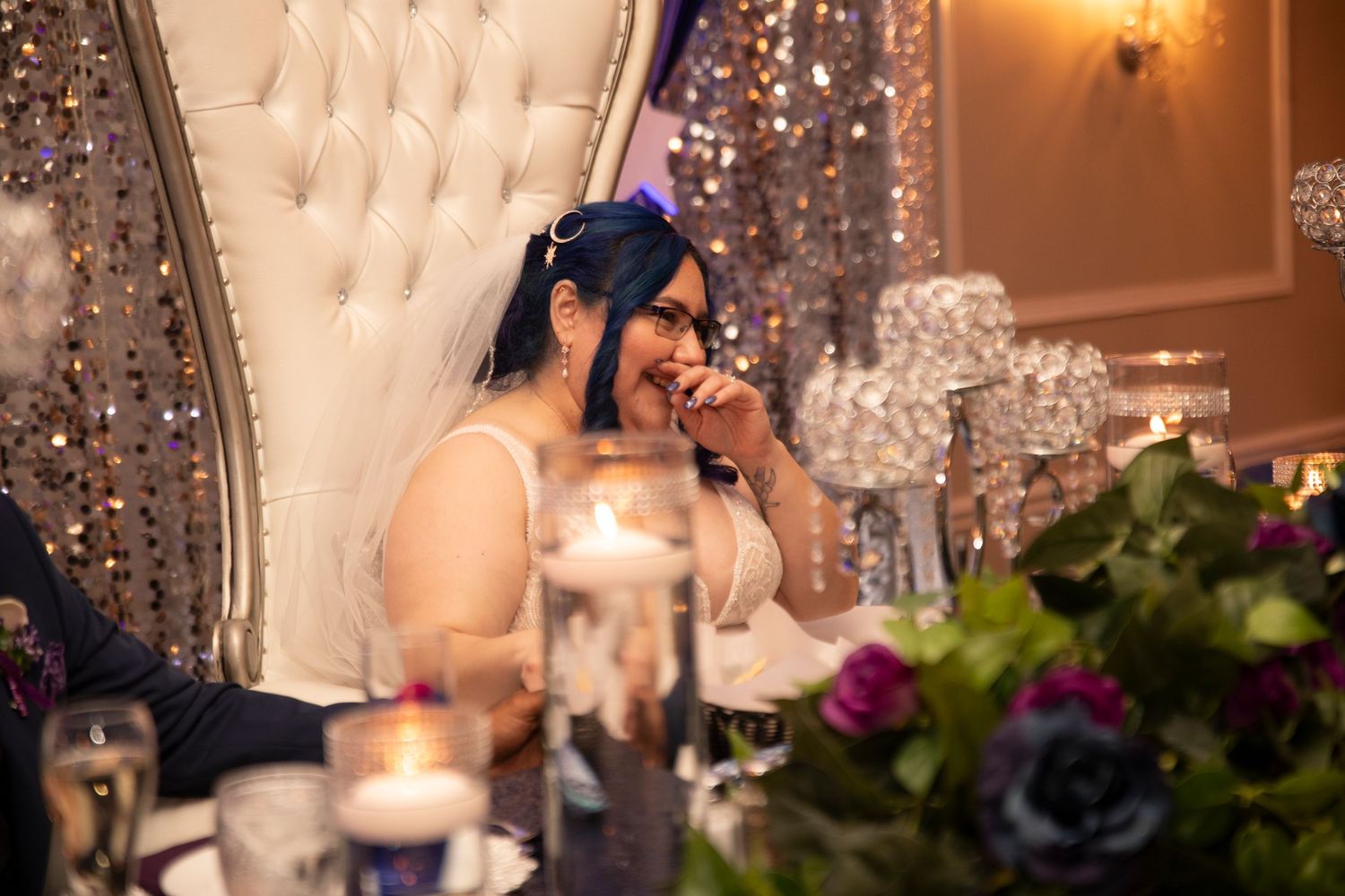 Elegant wedding reception venue decorated with crystal chandeliers, candles and floral centerpieces on dining tables.