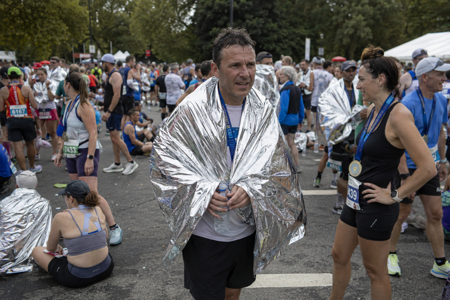 Marathon finisher wrapped in silver thermal blanket at race finish area.