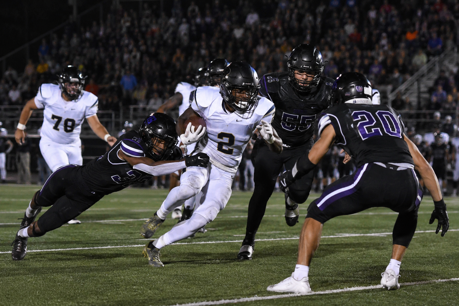Football player in white uniform breaks through defenders during an intense night game.