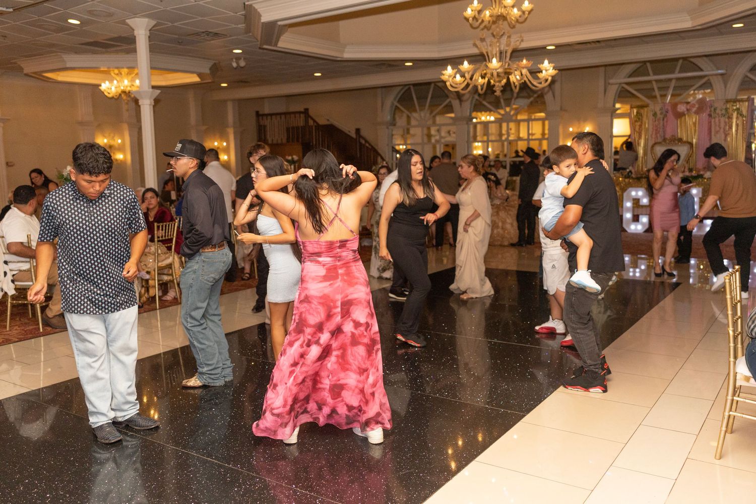 Guests dancing on a black marble floor at an elegant wedding reception in a grand ballroom.