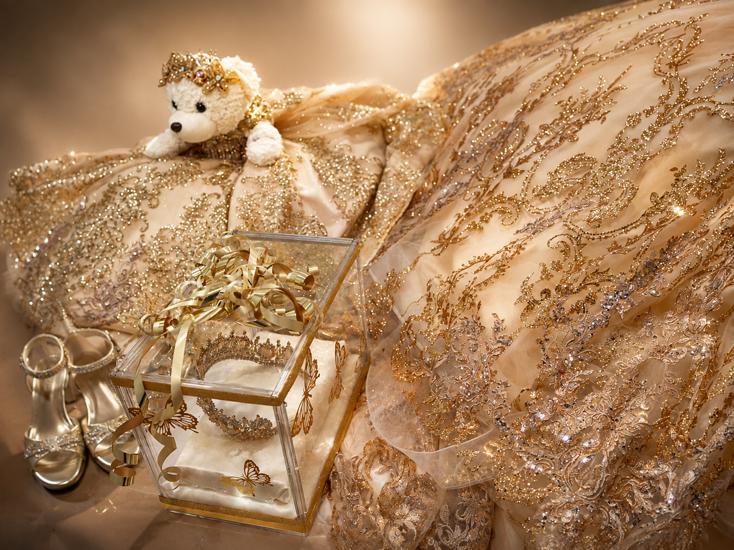 Elegant gold lace fabric with sparkling embroidery, a teddy bear, glass box, and decorative accessories in a luxurious arrangement.