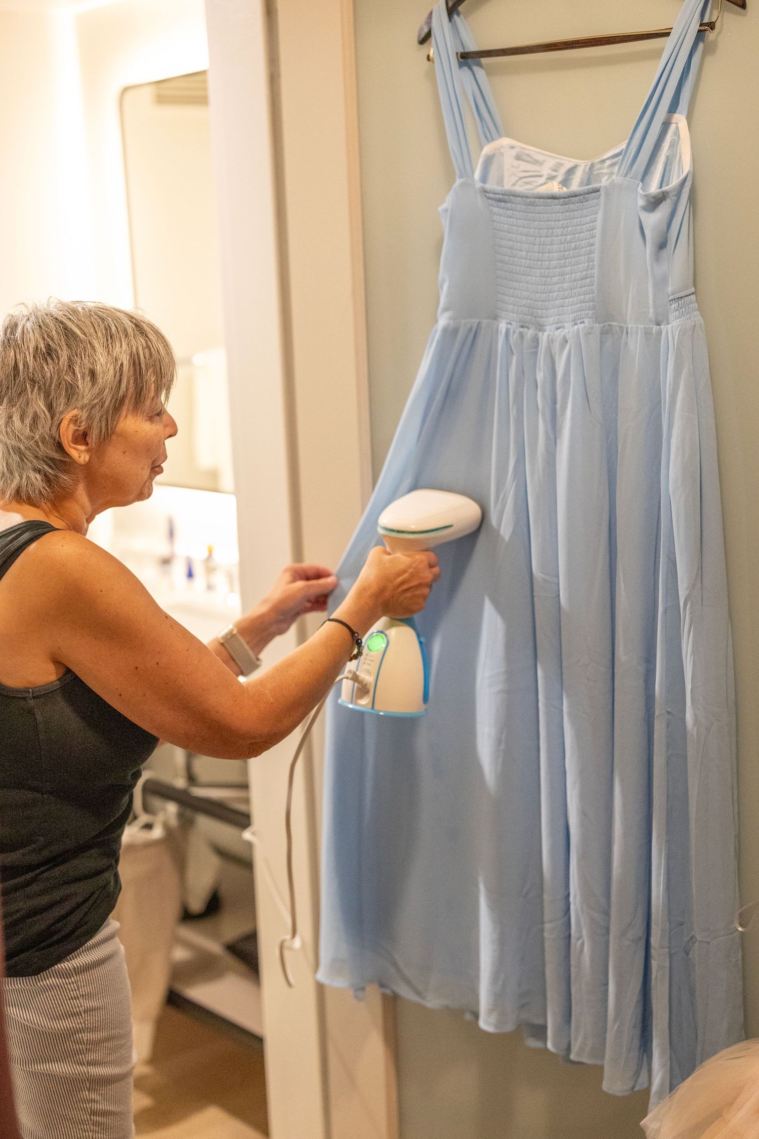 Woman steaming a light blue dress on a hanger using a handheld garment steamer indoors.