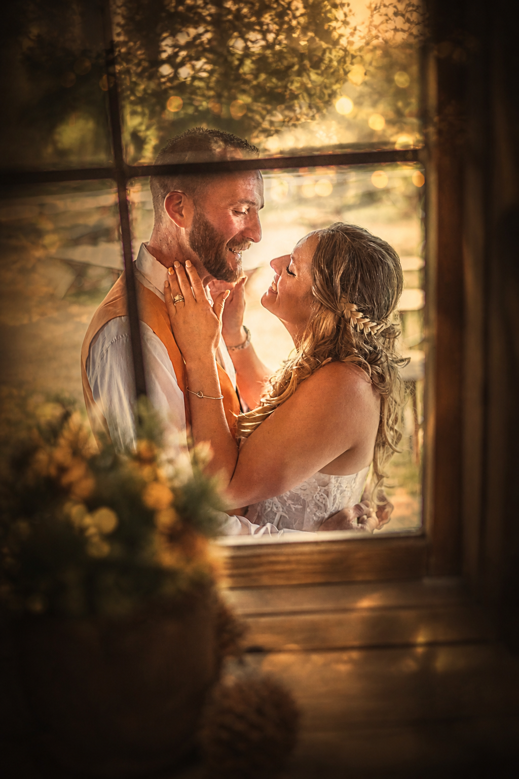 A joyful bride and groom share a romantic moment framed by a rustic wooden window at golden hour.