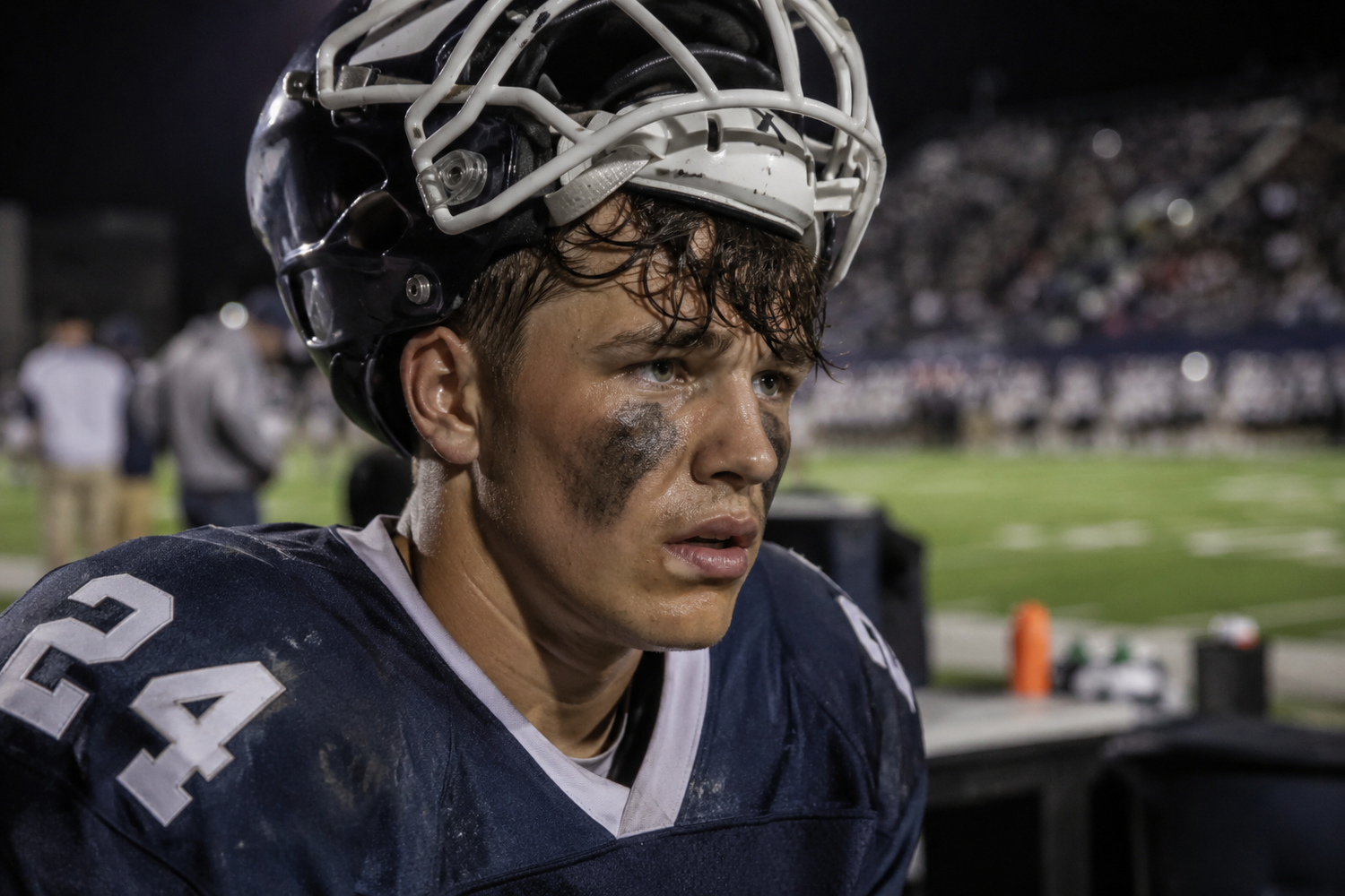 Exhausted football player #24 in a dirty uniform and helmet after a tough game under stadium lights.