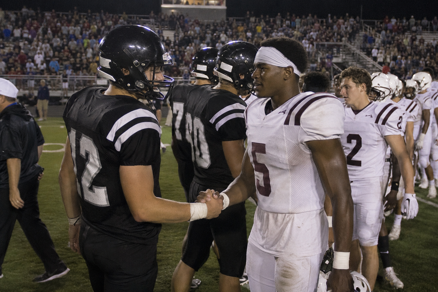 High school football players from opposing teams shake hands on the field after a competitive night game.