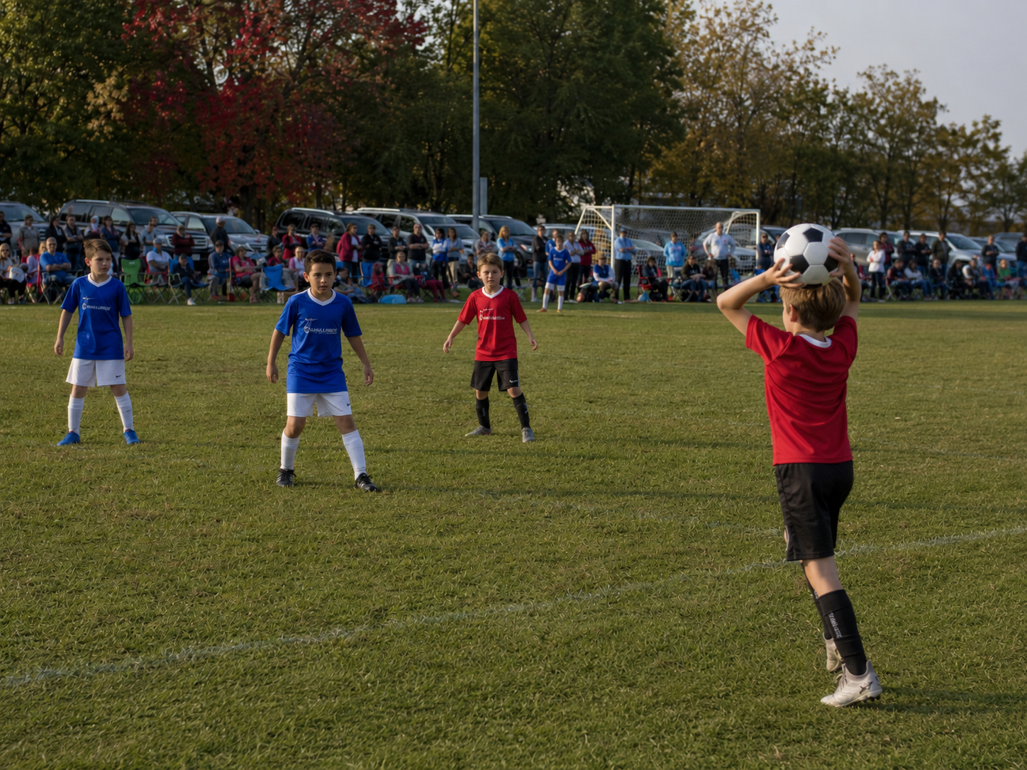 Kids playing soccer on a green field during a youth soccer game with spectators watching in the background.