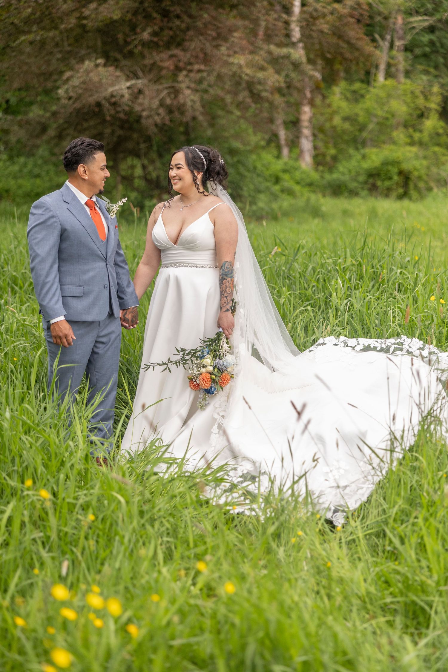 A couple in wedding attire poses together in a lush green meadow with wildflowers on their special day.