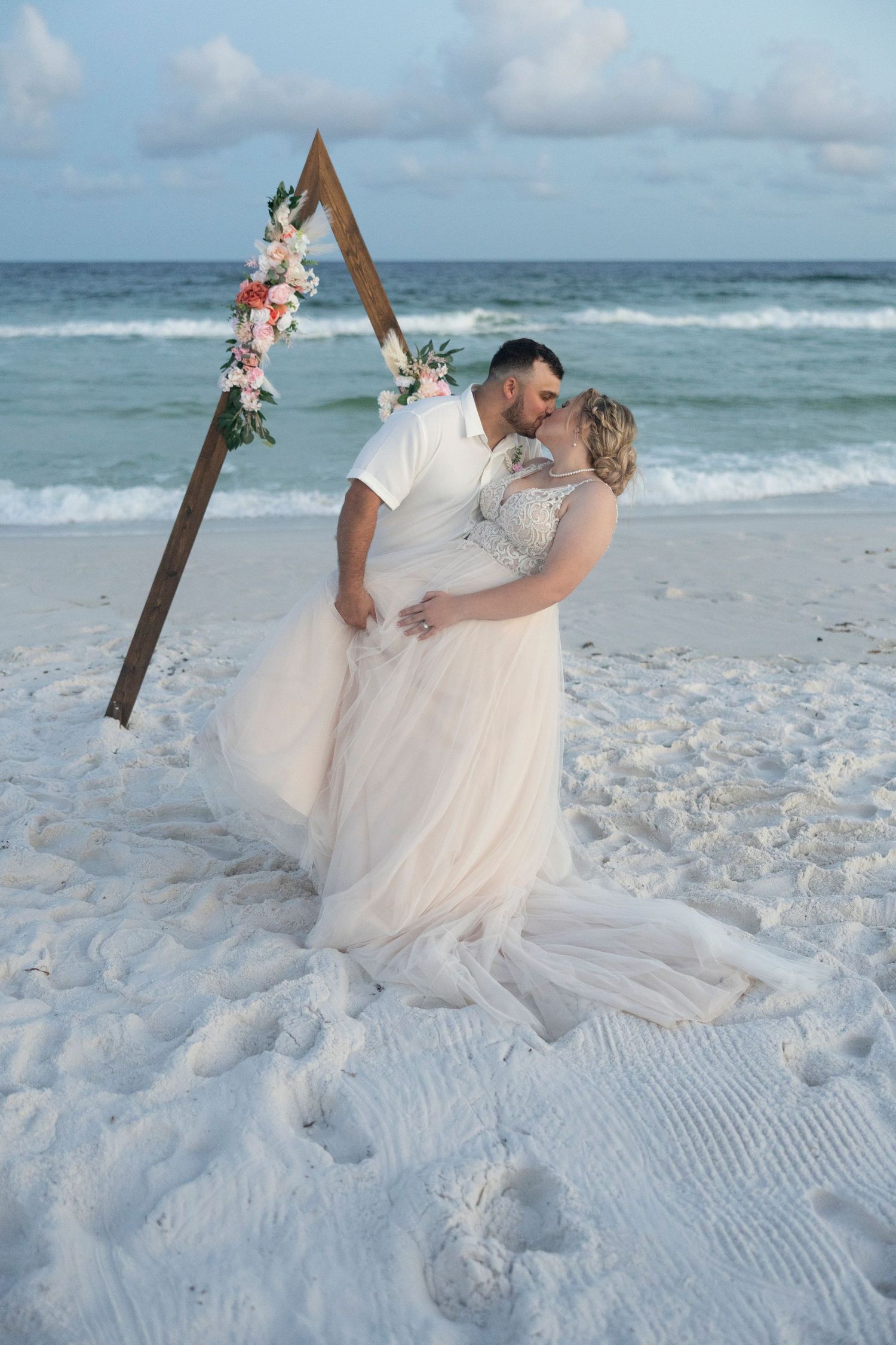 Romantic beach wedding photoshoot with couple dancing on white sand as ocean waves roll in the background.