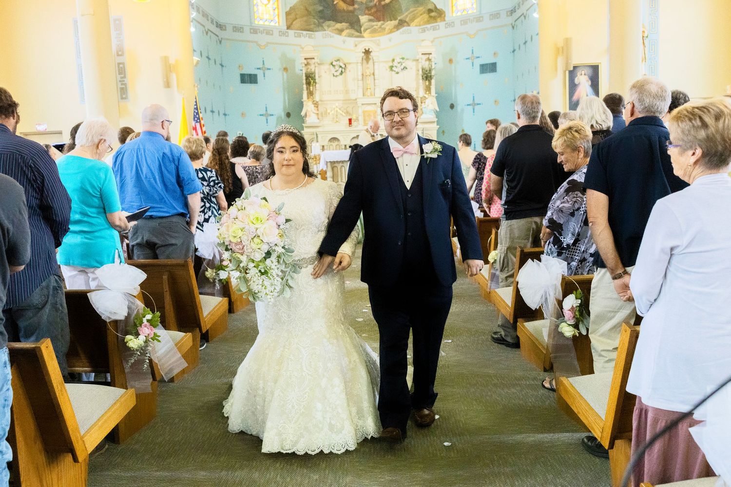 Wedding guests mingle and socialize in a church aisle during a joyous celebration.