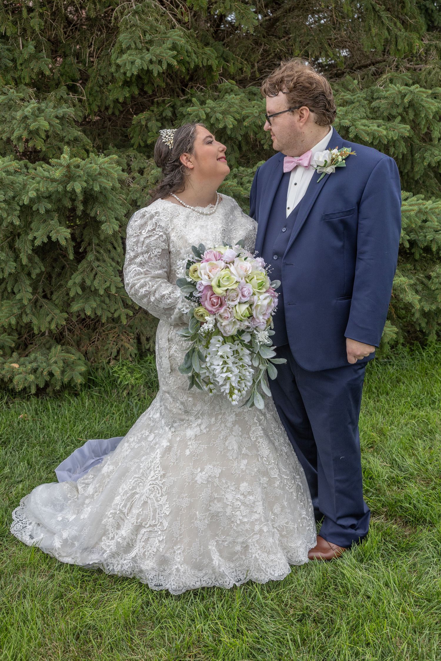 A couple in wedding attire share a romantic moment outdoors with lush greenery in the background.