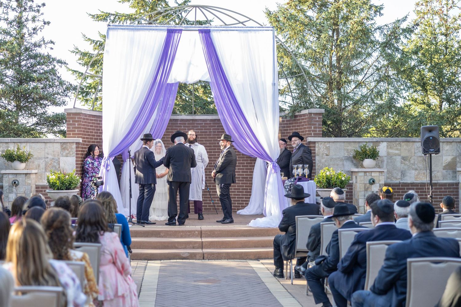 Outdoor wedding ceremony setup with purple draping and white chairs arranged in rows on a sunny day.