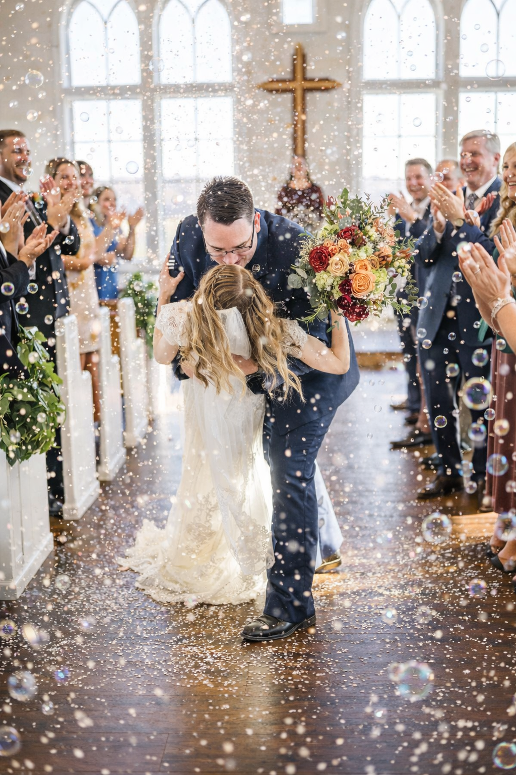 A couple shares their first kiss as newlyweds in a church while guests throw confetti during a joyful wedding ceremony.