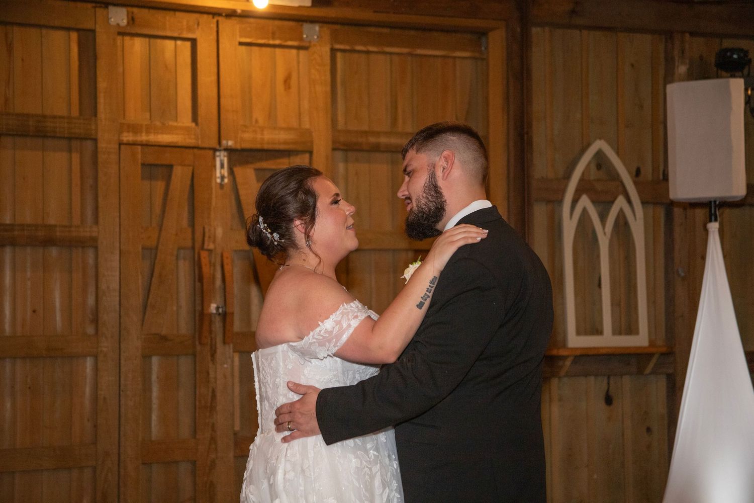 A couple shares their first dance together in a rustic wooden barn with gothic-style windows at their wedding reception.