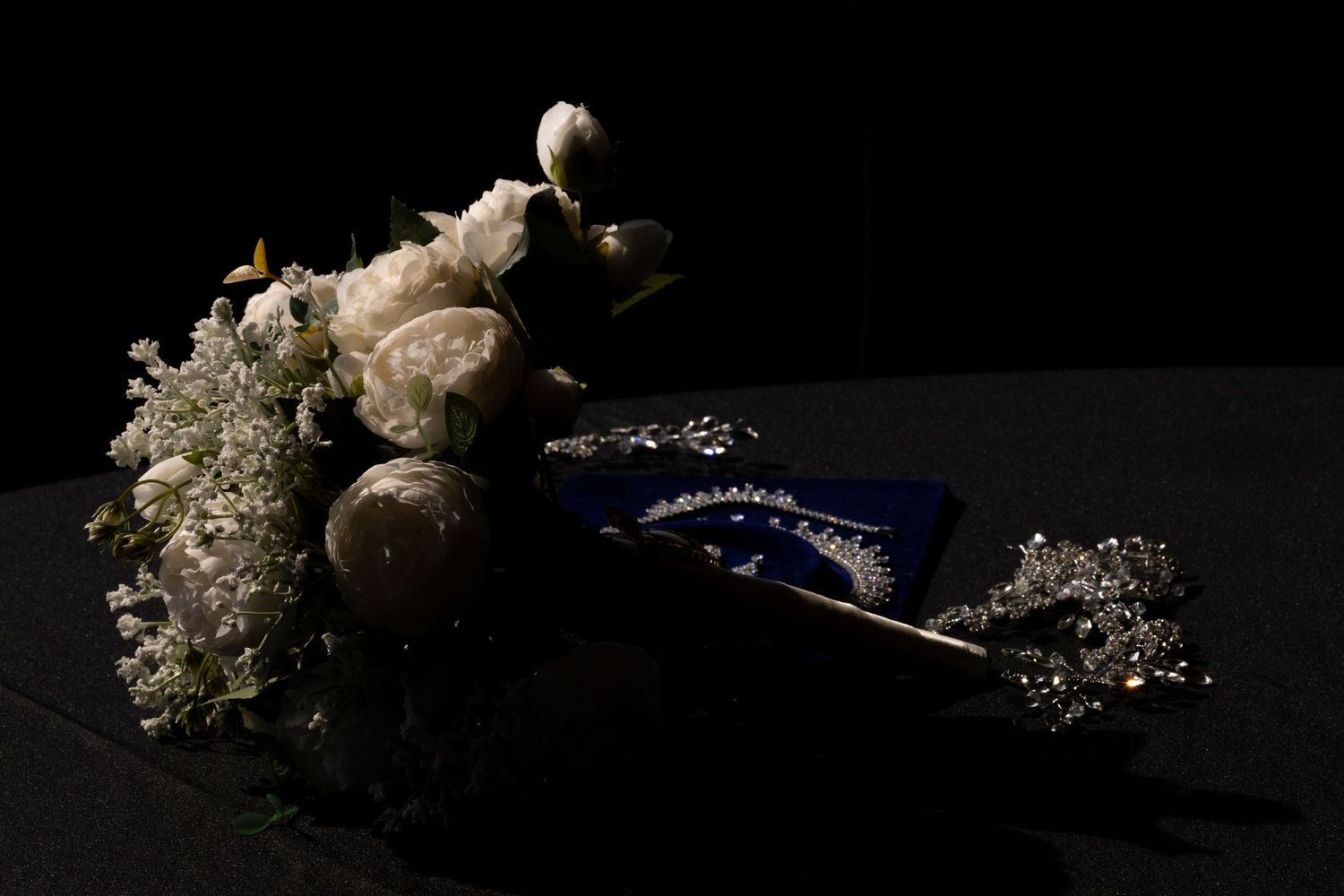 A series of dark, moody still life photographs showing white flowers and blue fabric against black backgrounds.