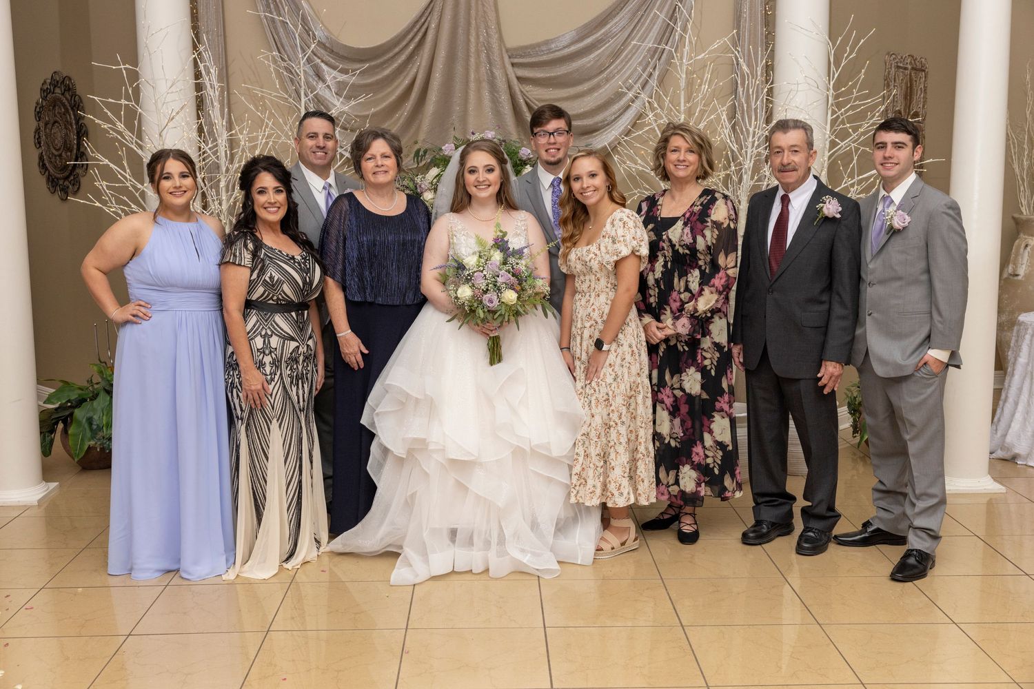 Wedding party in formal attire poses together against a draped backdrop.