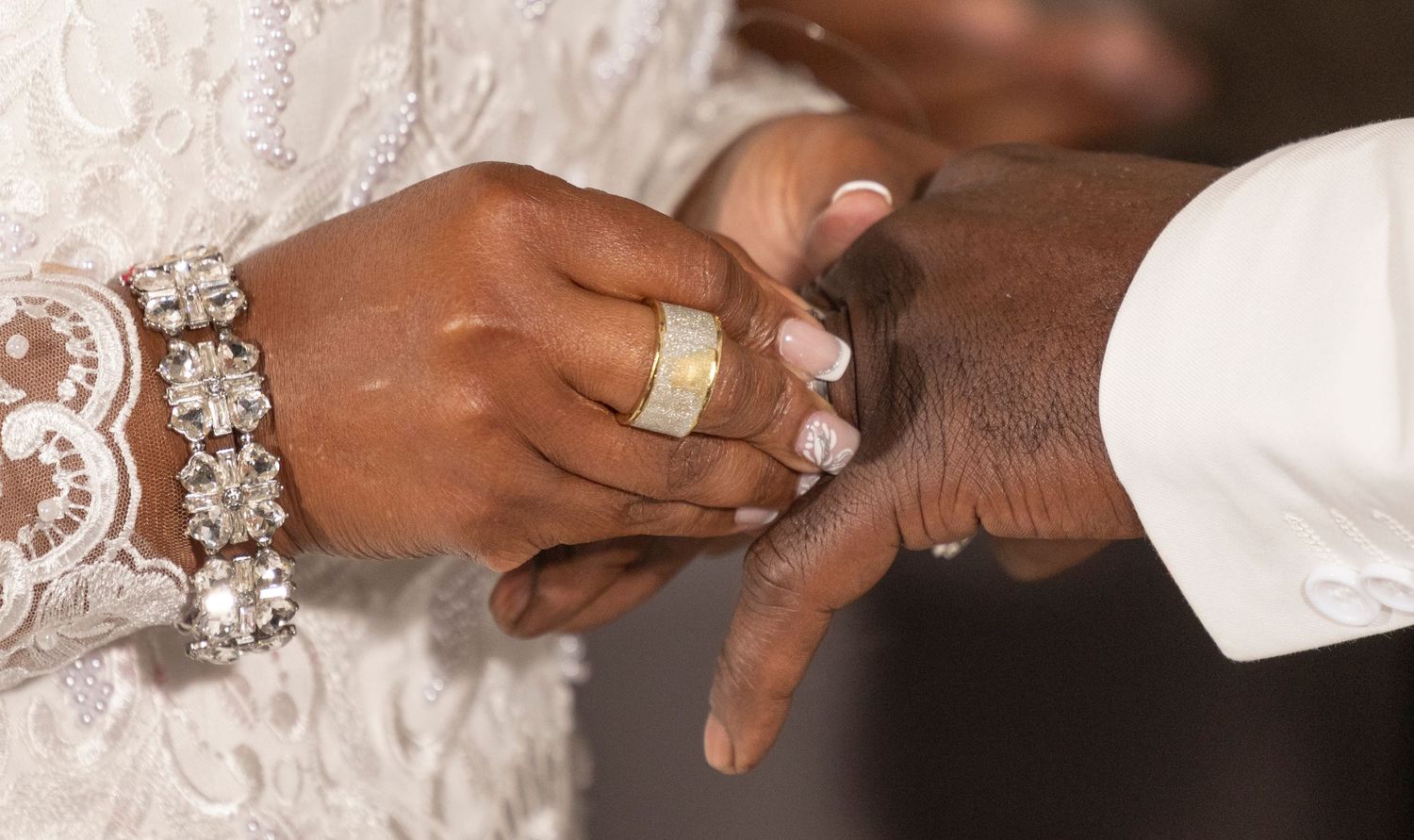 Close-up of a wedding ring exchange ceremony, bride in lace dress with diamond bracelet.