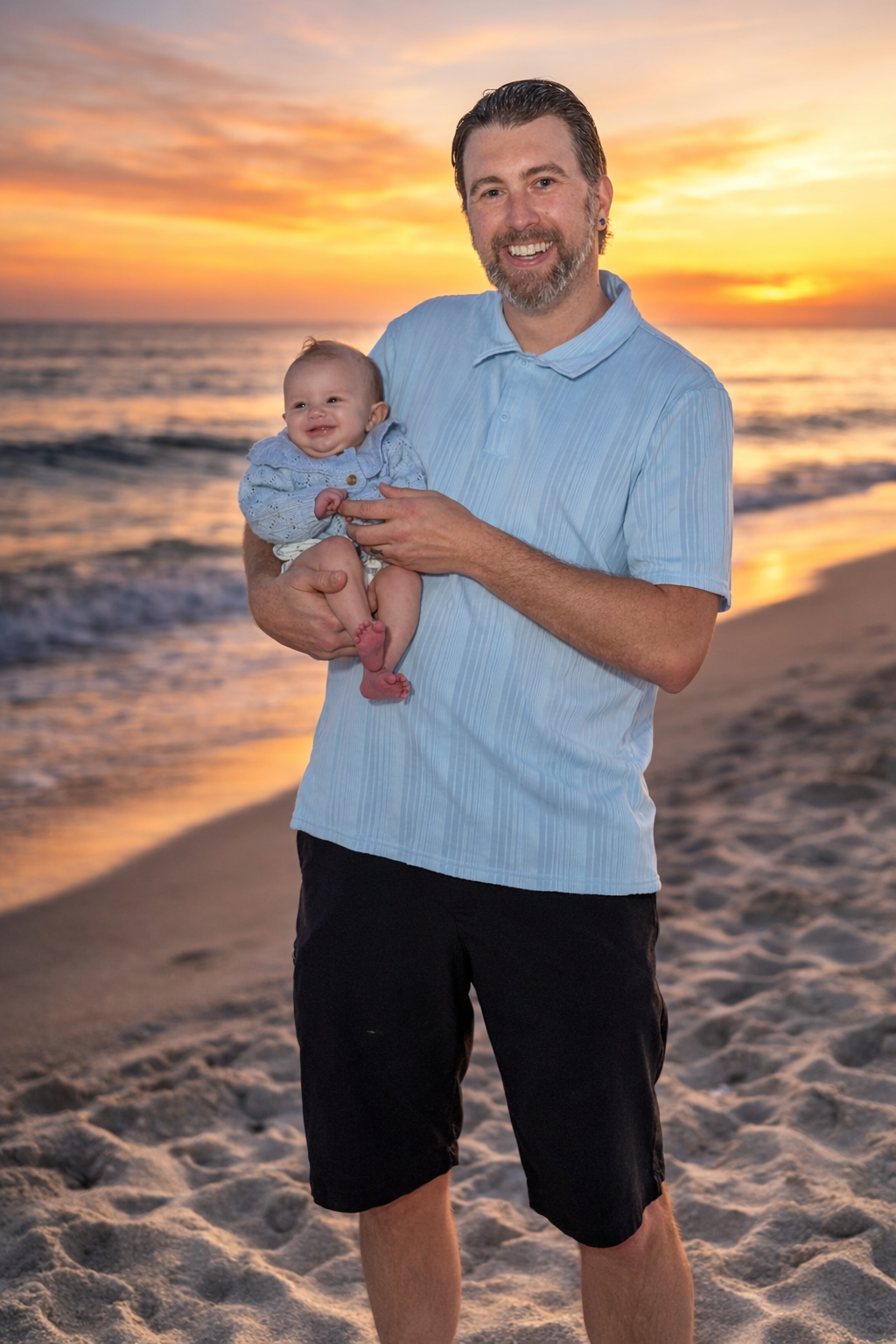 A parent and baby share tender moments on a sandy beach at sunset with golden orange skies in the background.