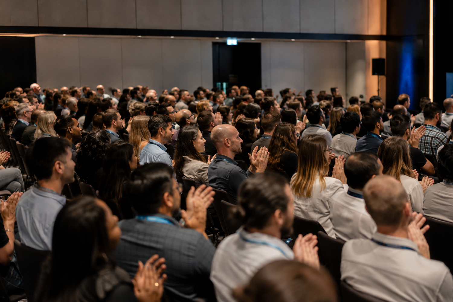 Large audience applauding at a professional conference event in a modern venue.