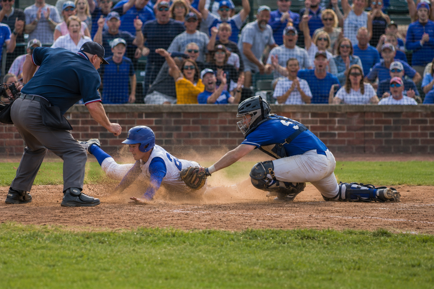 Baseball player slides into home plate as catcher attempts tag while umpire watches closely.