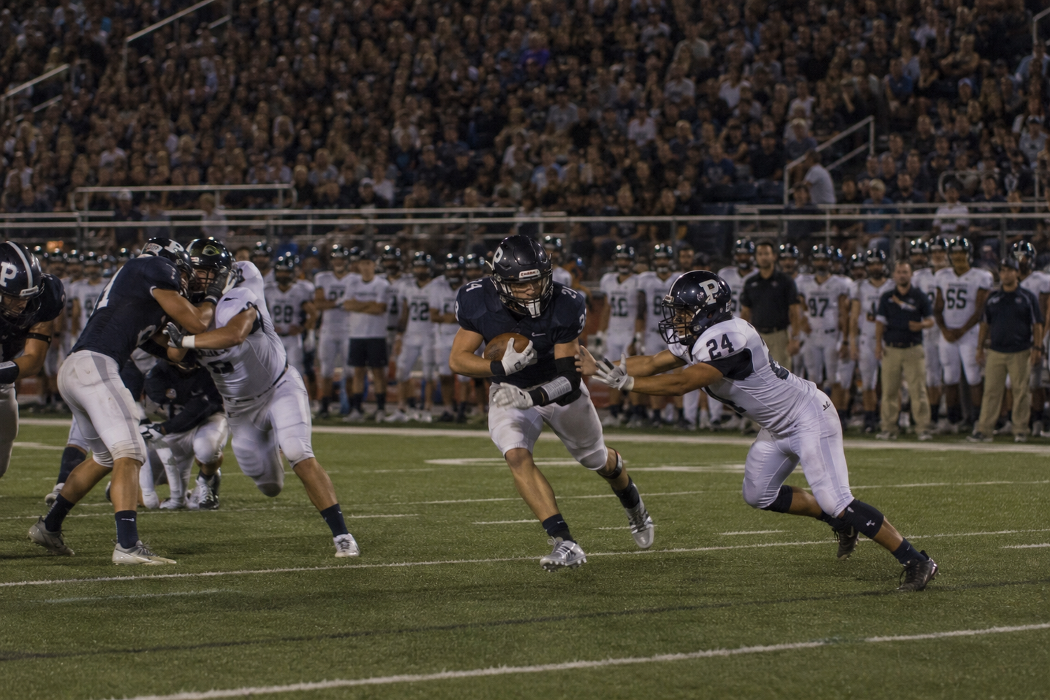 Football player breaks through defensive line during a night game under bright stadium lights.