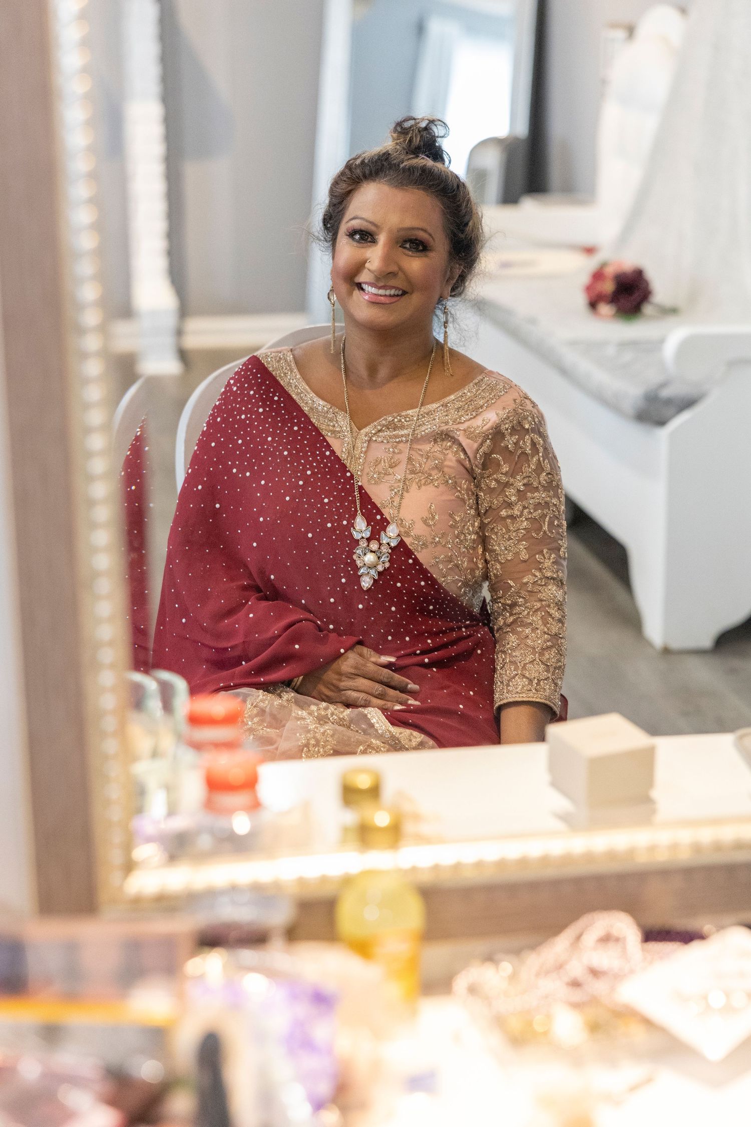 Someone wearing a burgundy and gold sequined dress smiles while seated at an elegant event with candlelit decor.