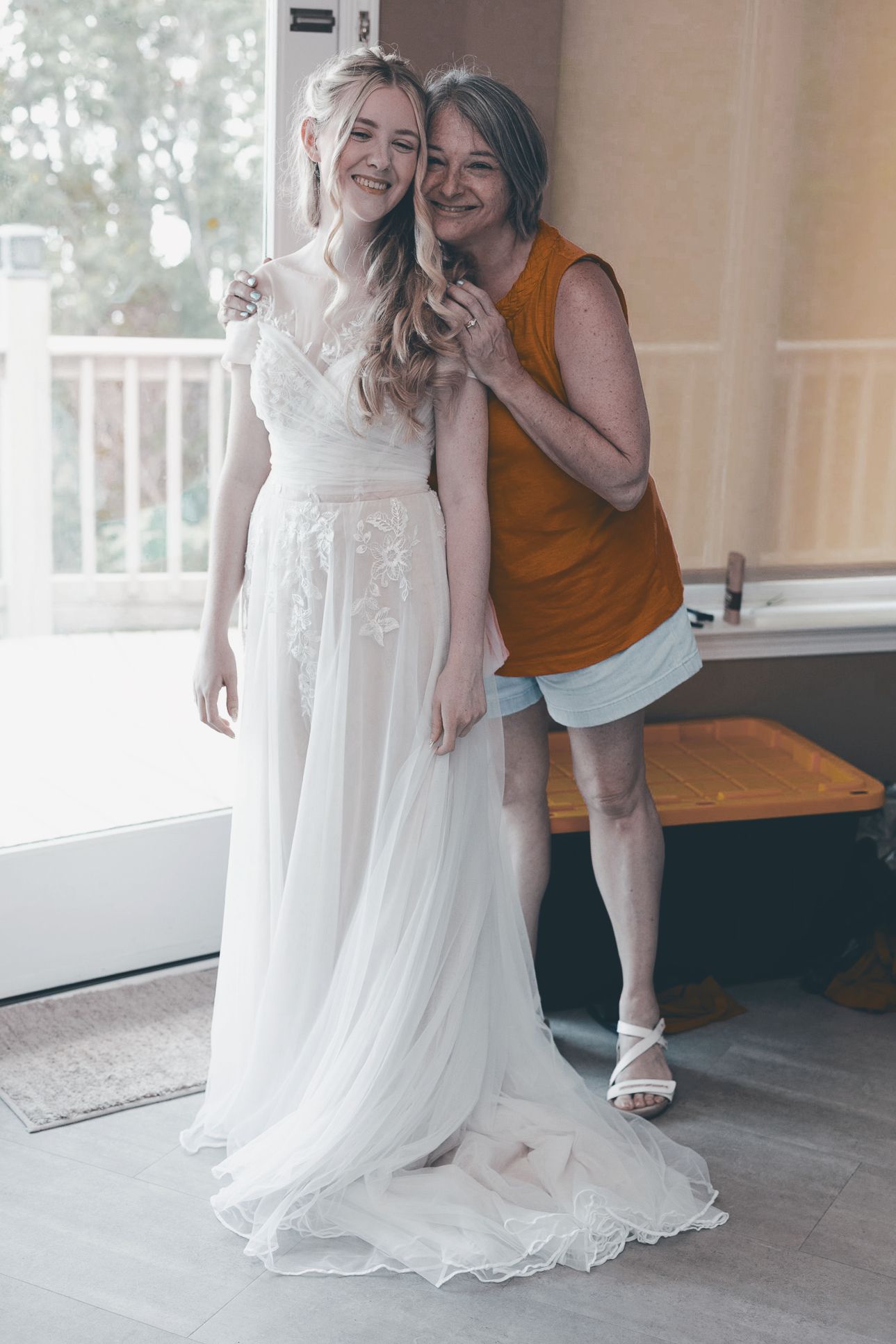 A touching moment captured during wedding preparations shows a bride in a flowing white gown with someone in a rust-colored top.