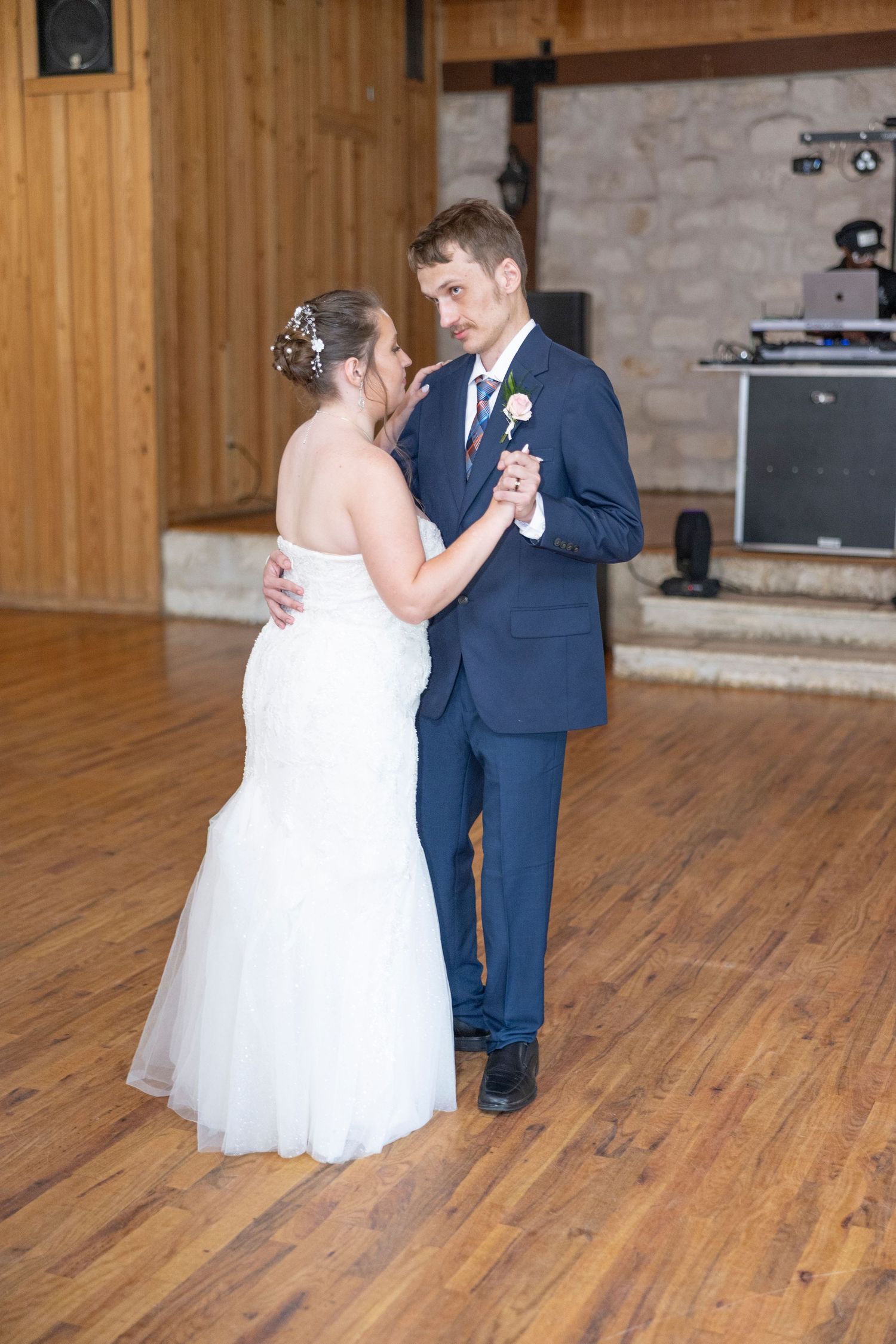 A couple shares their first dance together at their wedding reception on a wooden dance floor in a rustic venue.