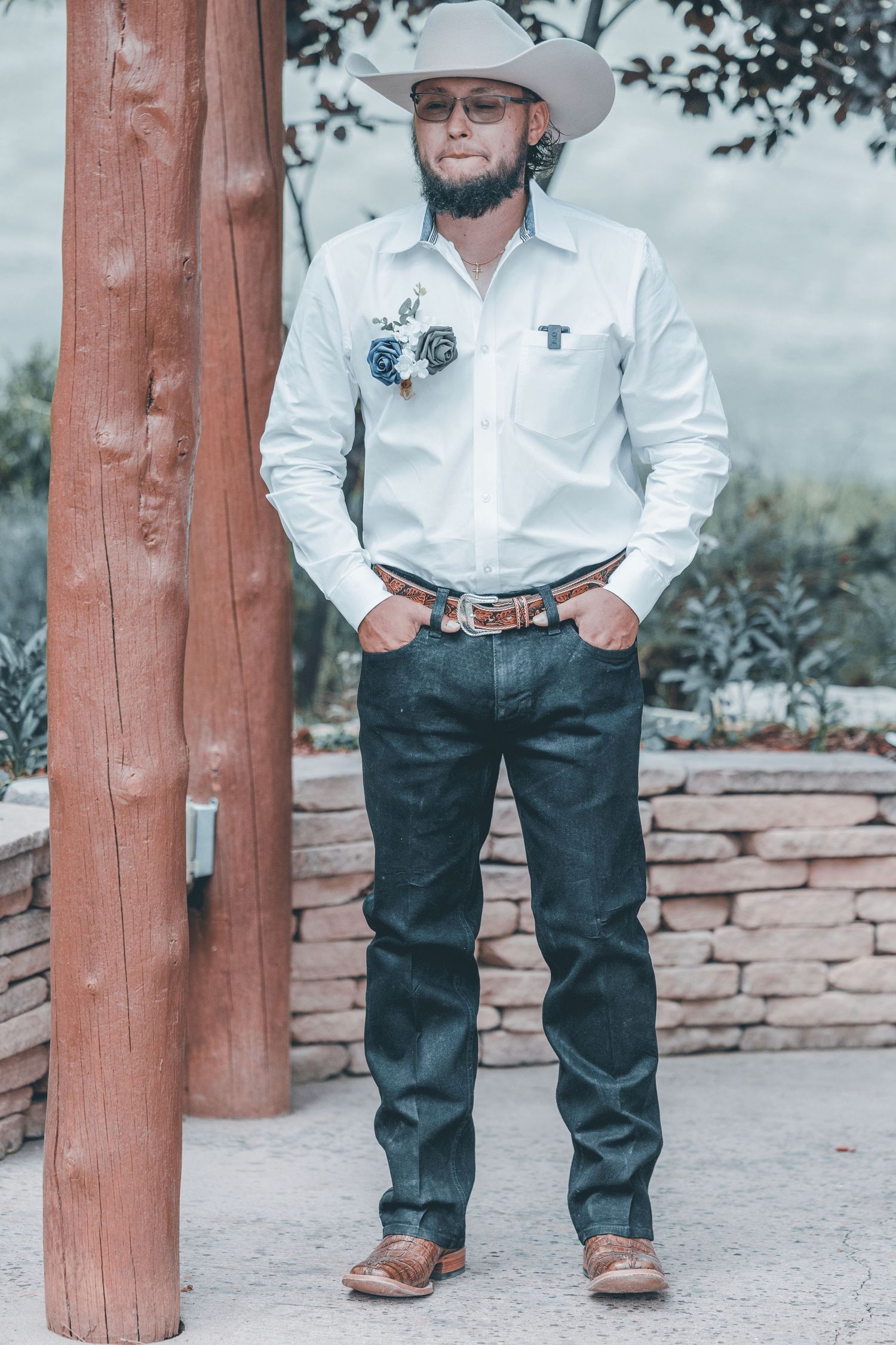 Western-style boots and jeans shown in detail against rustic wooden posts and stone wall background.