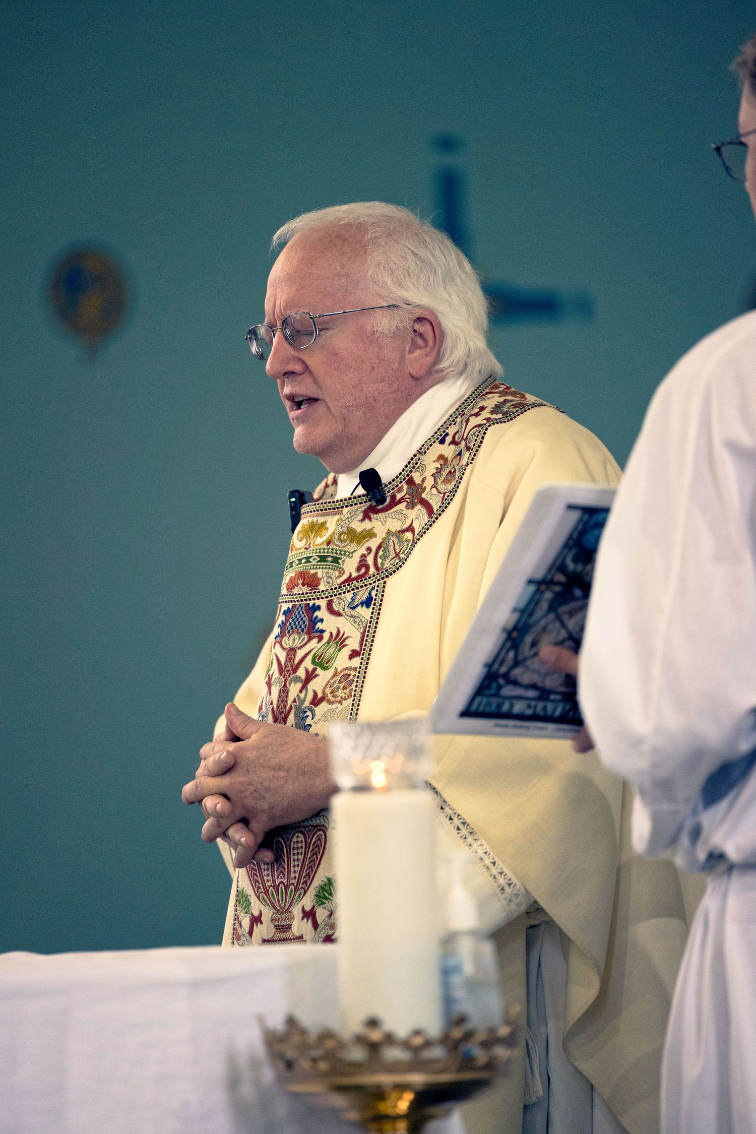 A person in religious vestments and a floral stole laughs joyfully during a ceremonial service.