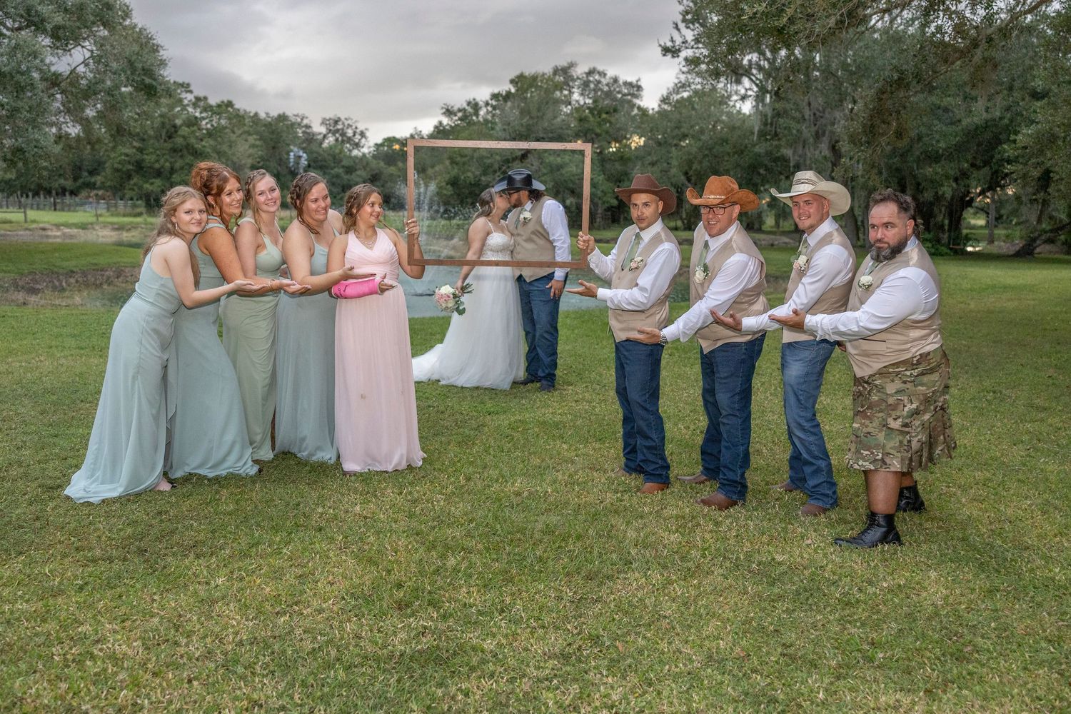 A wedding party poses playfully in a grassy field wearing coordinated blue, pink and denim outfits.