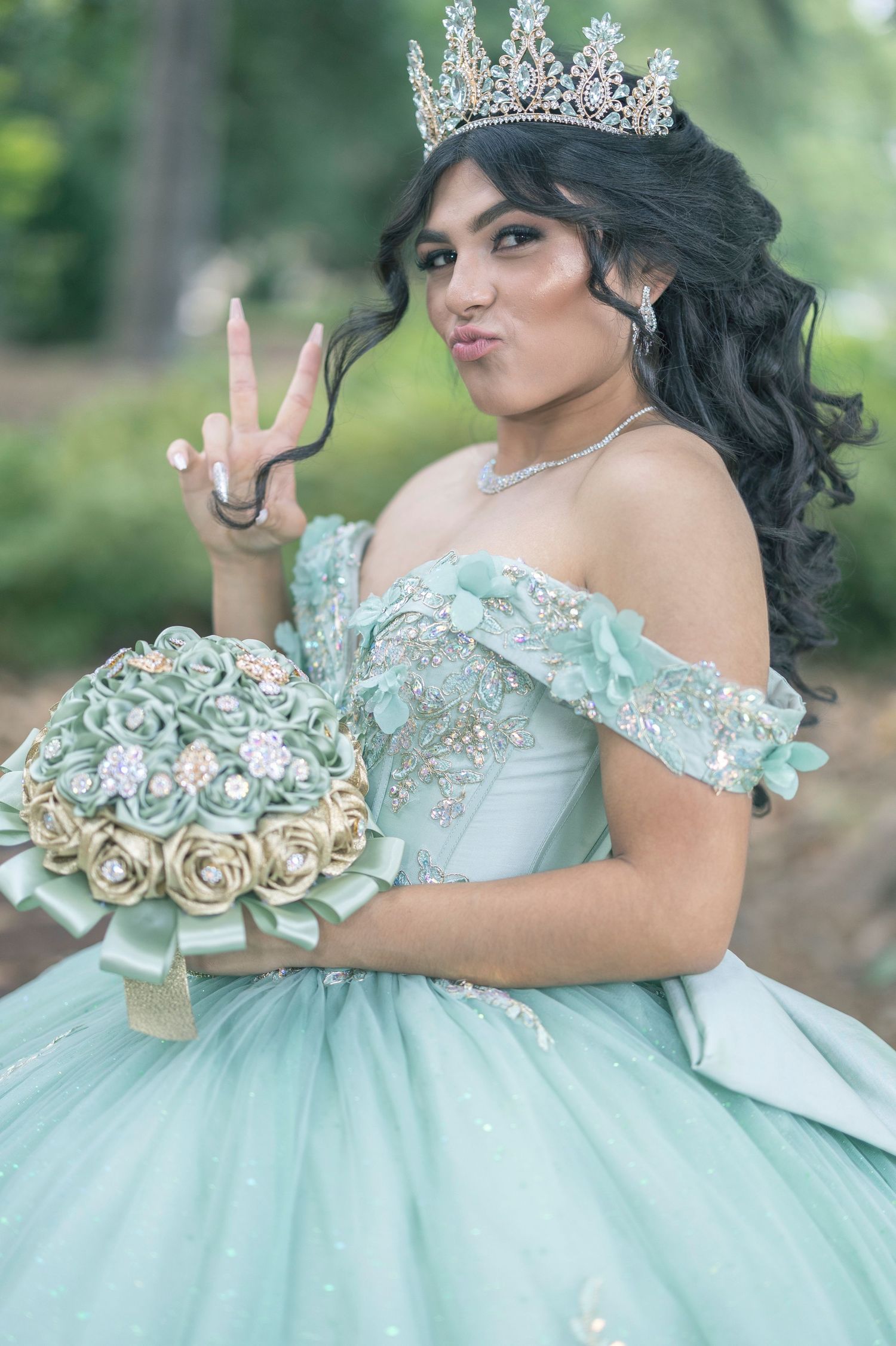 A mint green quinceañera ball gown with off-shoulder design and floral details is showcased in an outdoor setting.