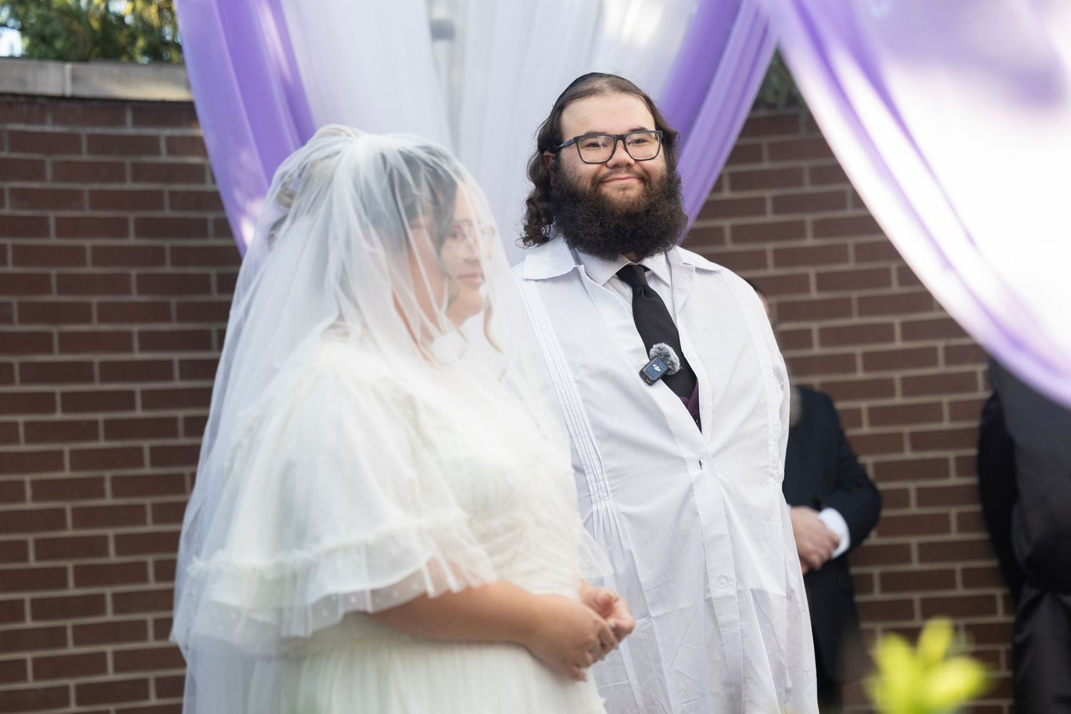 Wedding ceremony setup with purple drapes against brick wall and white decorations.