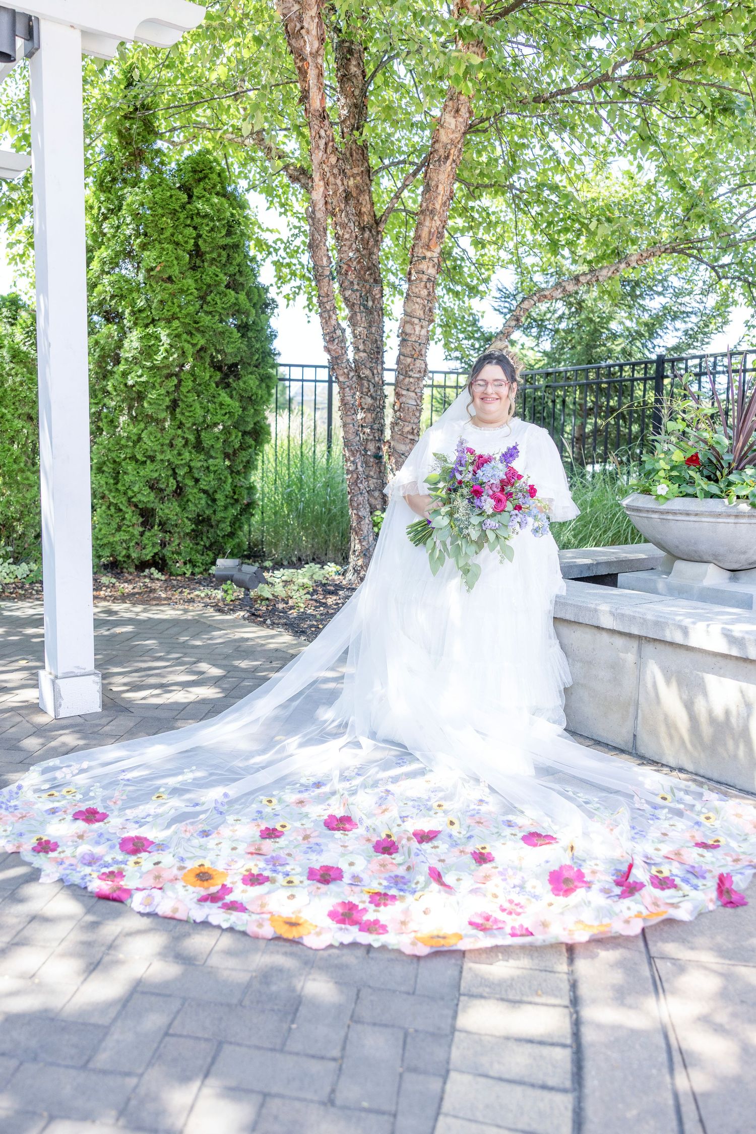A stunning wedding dress with pink and orange floral petals decorating the long flowing train in an outdoor garden setting.