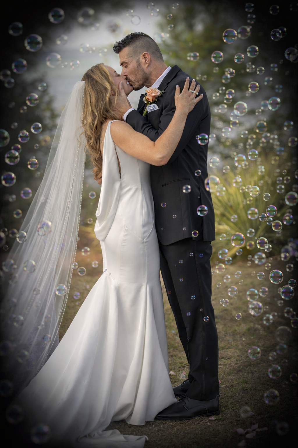 Bride and groom share a romantic kiss surrounded by floating bubbles outdoors on their wedding day.