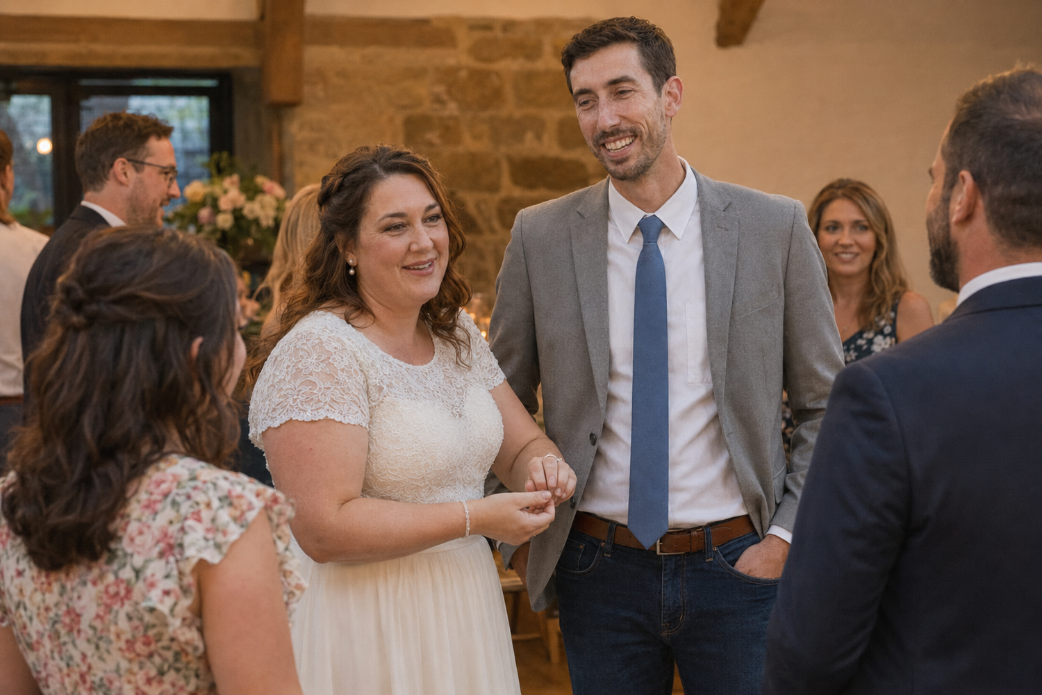 Bride and groom smiling and chatting with wedding guests in a rustic barn venue.