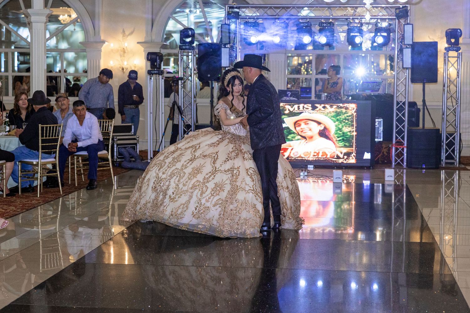 A couple shares a dance at a quinceañera celebration in an elegant ballroom with a large LED screen backdrop.