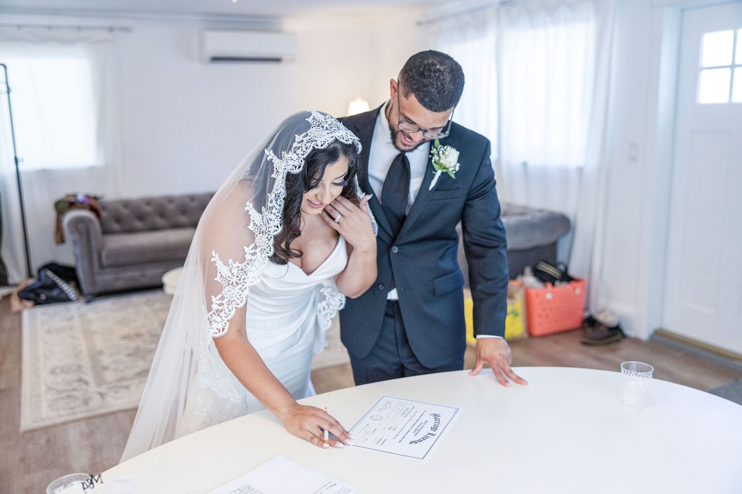 Couple signing marriage documents at a wedding ceremony while seated at a table in a bright room.
