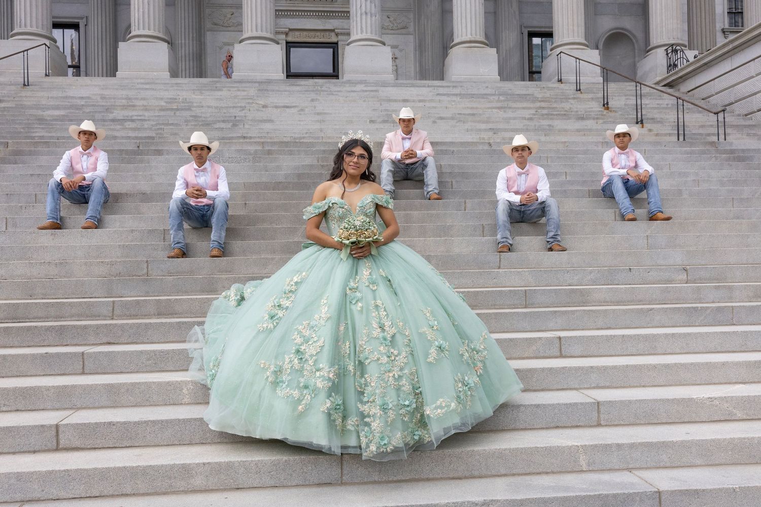 A woman in a mint green quinceanera dress poses on grand stone steps for a photo session.