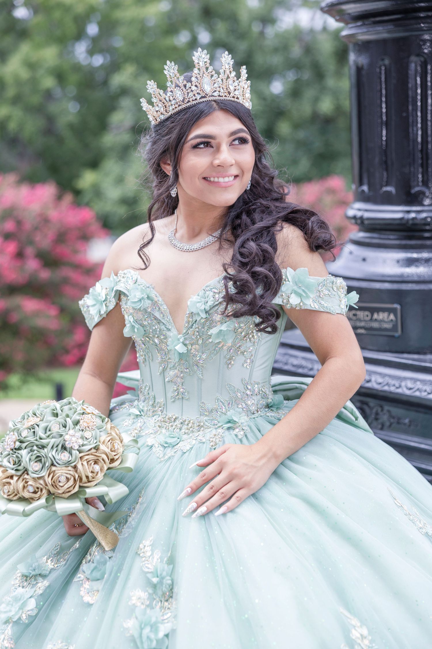 A stunning mint green quinceanera dress with off-shoulder details and crystal crown photographed in an outdoor setting.