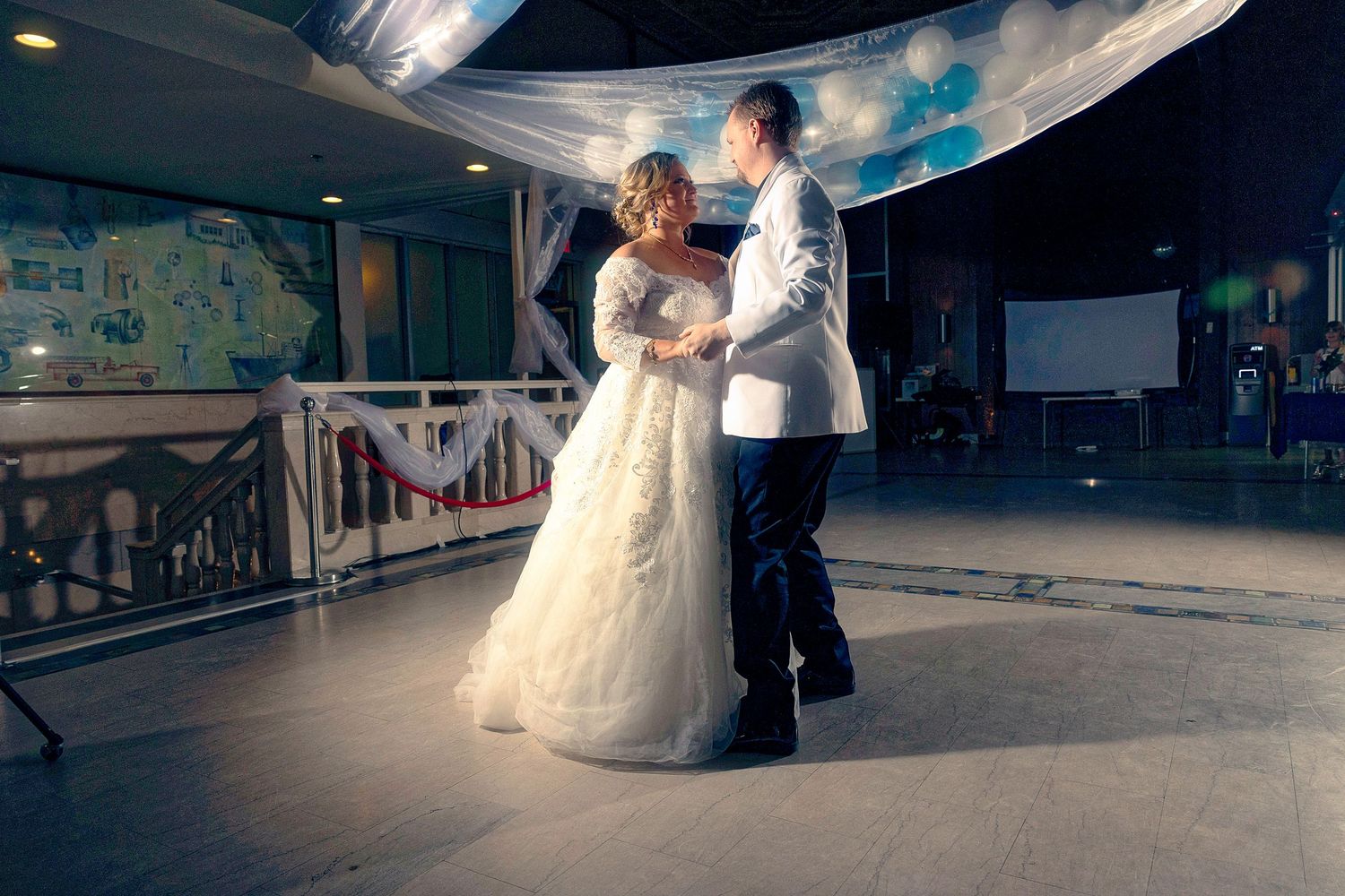 Bride and groom sharing their first dance at wedding reception, bride in white gown, groom in white jacket.