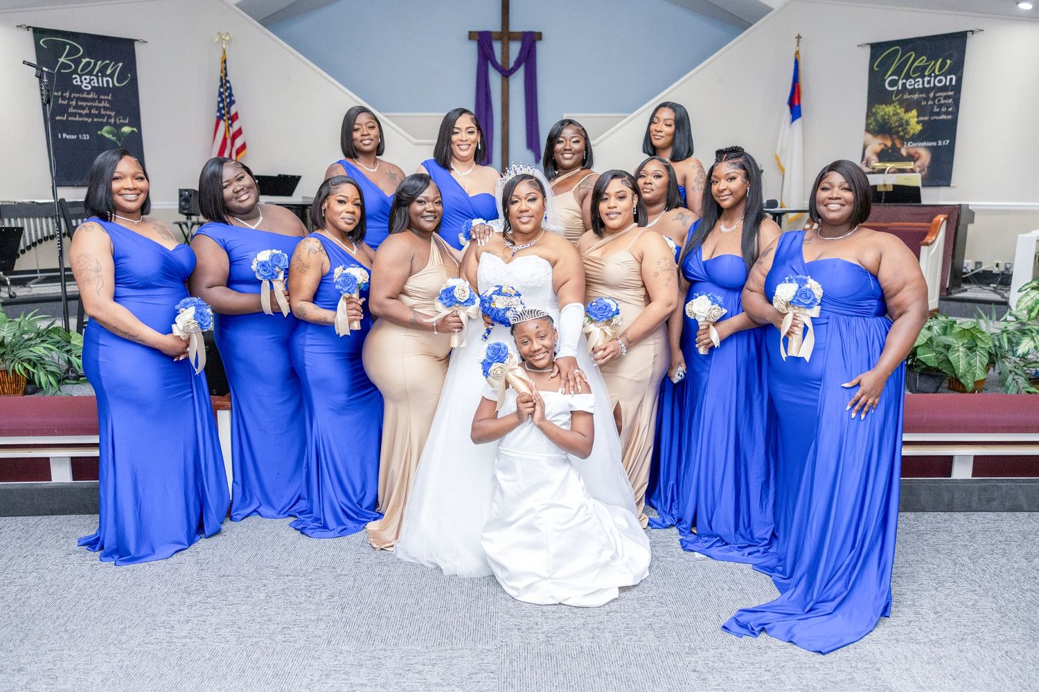 Bride in white gown poses with bridesmaids in royal blue dresses holding bouquets inside a decorated church.