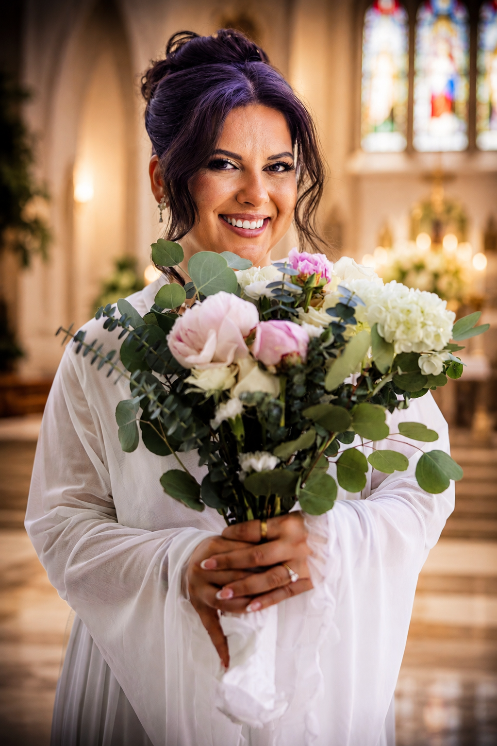 Smiling bride with purple hair holding a bouquet of roses and eucalyptus in a church.